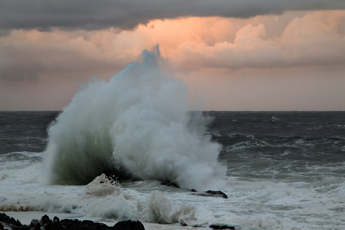 A large wave breaking against a rock splashing up